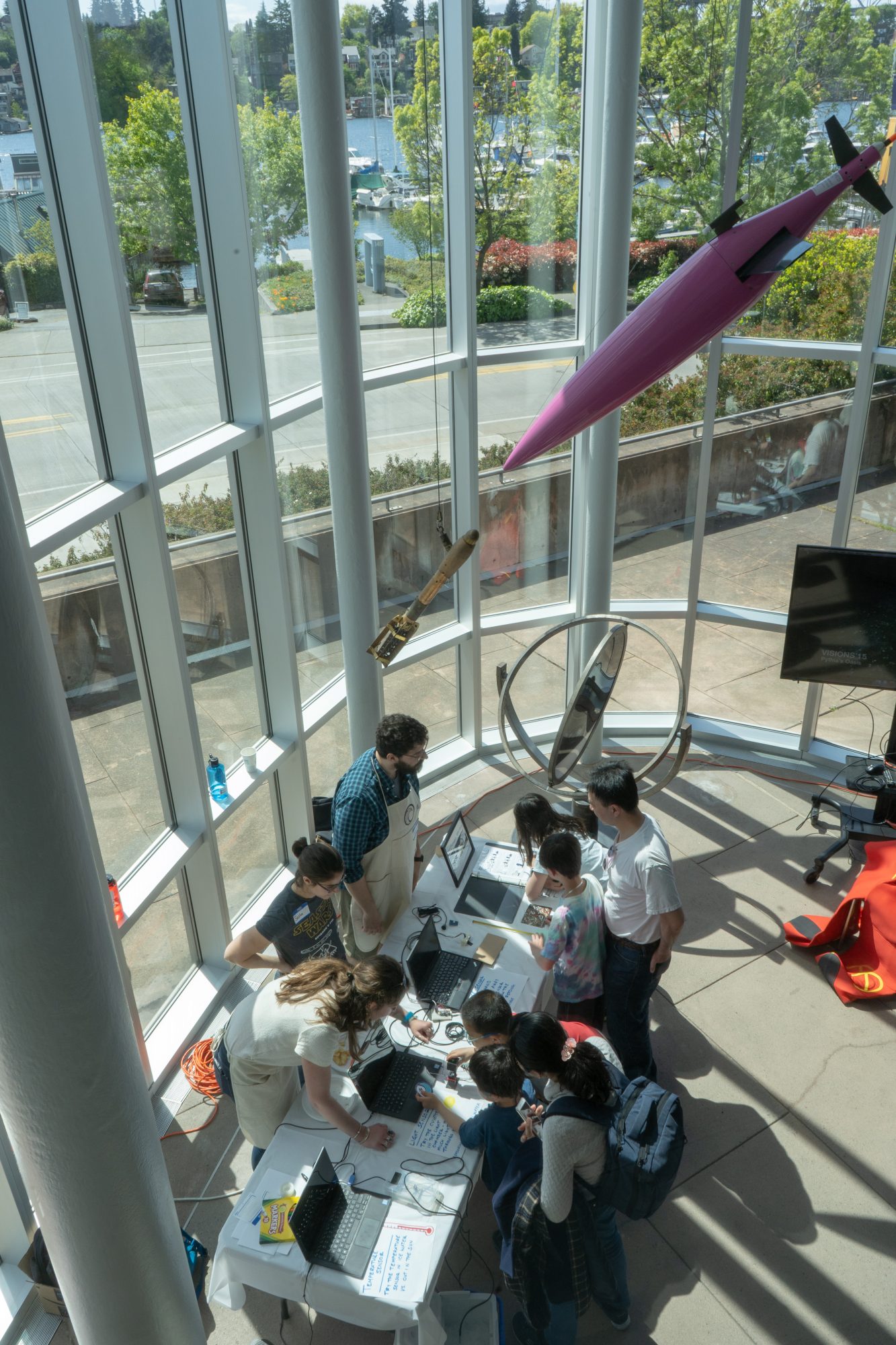 An aerial shot of people around an exhibition table in a building with lots of windows.
