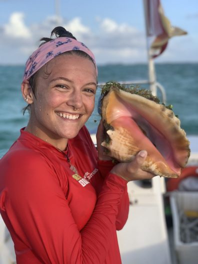 Student hold a queen conch on a boat