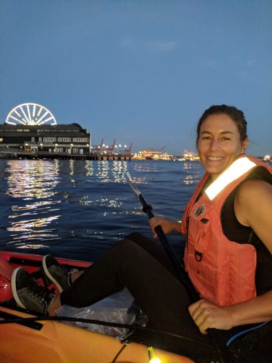 Kerry kayaking along Seattle's seawall at night. The Seattle Great Wheel in the background lit up