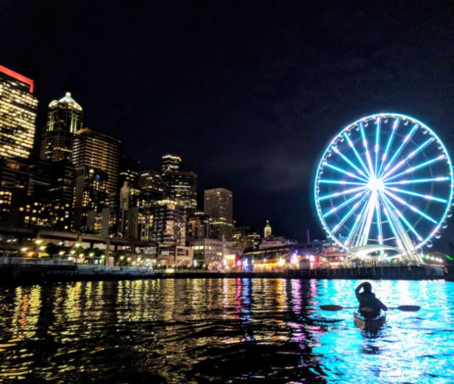 Kerry kayaking along Seattle's seawall at night. The Seattle Great Wheel in the background lit up