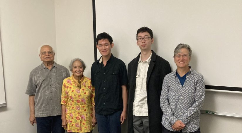 Five people stand side by side in front of a whiteboard, smiling into the camera.