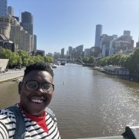 Ashley smiles into the camera while the background shows a cityscape with a river running through it.