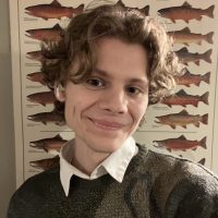 Eli Nettlebeck, an undergraduate student at SAFS, takes a selfie, with a poster displaying different types of fish on the wall behind.