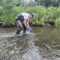Ryan crouches down in a river collecting eDNA.
