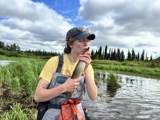 Emma kisses a fish while standing in a lake.