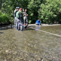 A group of students stand in a river with a white rope strung across.