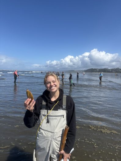 Larkin Stodolnic stands on a beach holding a clam