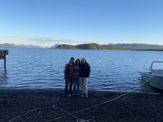 A group of students stand on the edge of a lake in Alaska.