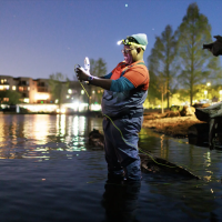 Ashley Townes stand in Lake Washington at night holding a remote controller to pilot an underwater remote-operated vehicle.