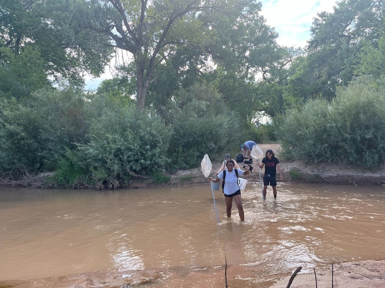 People wade across the Rio Grande river holding nets